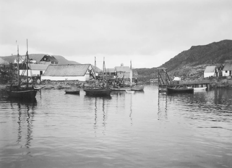 several sailboats moored in a bay with mountains and houses behind them