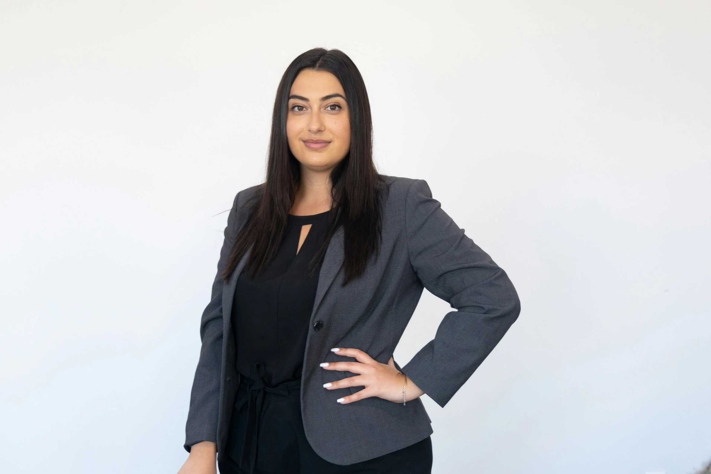 woman in business wear standing sideways against a white wall