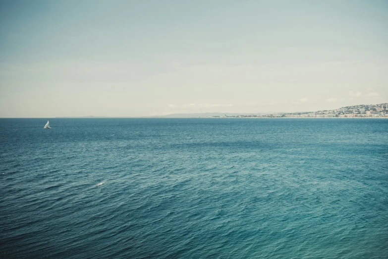 a sail boat floating on the ocean with mountains in the background