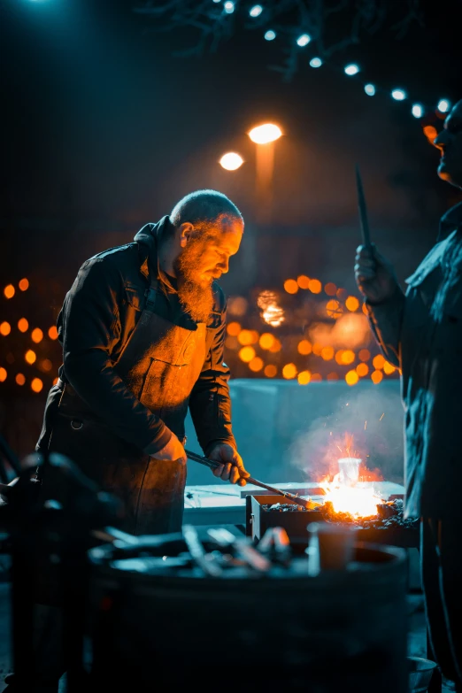 two men standing over a fire with dark background