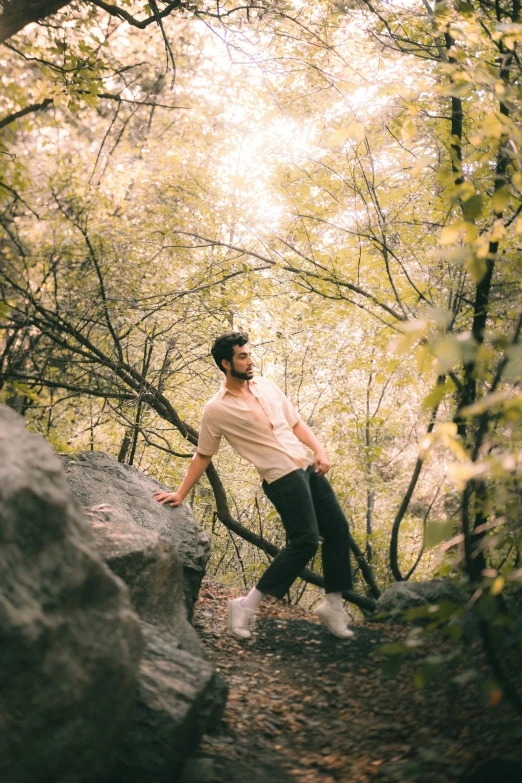 man climbing rock in wooded area with trees in the background