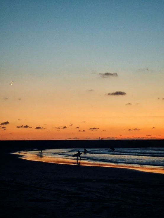 the sun sets on a beach as surfers walk into the water