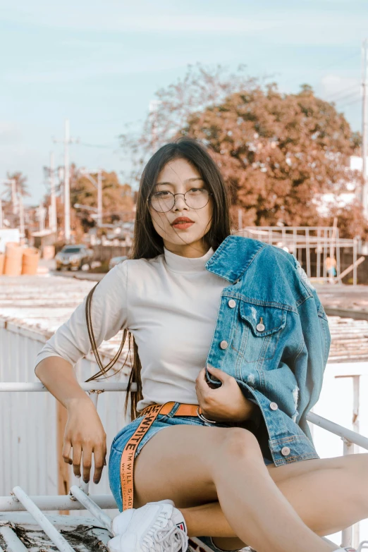 a woman sitting on top of a bench wearing a denim jacket