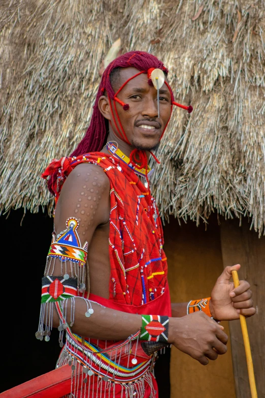 a man in a red outfit standing in front of a straw hut