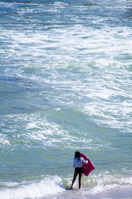 a girl is on the beach and is holding a pink surfboard