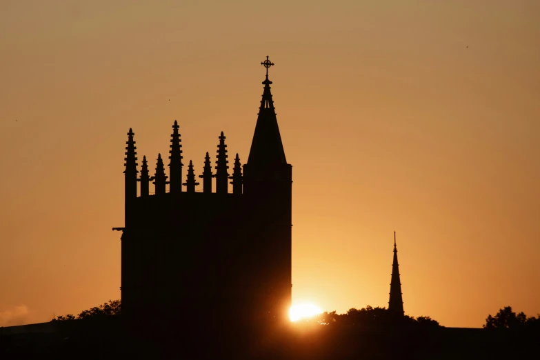 a cathedral spire is silhouetted against the sunset