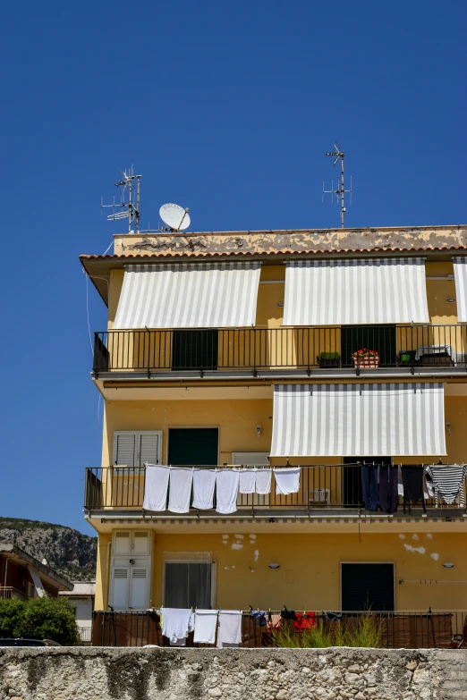 several laundry hung on the clothes line in front of a yellow building