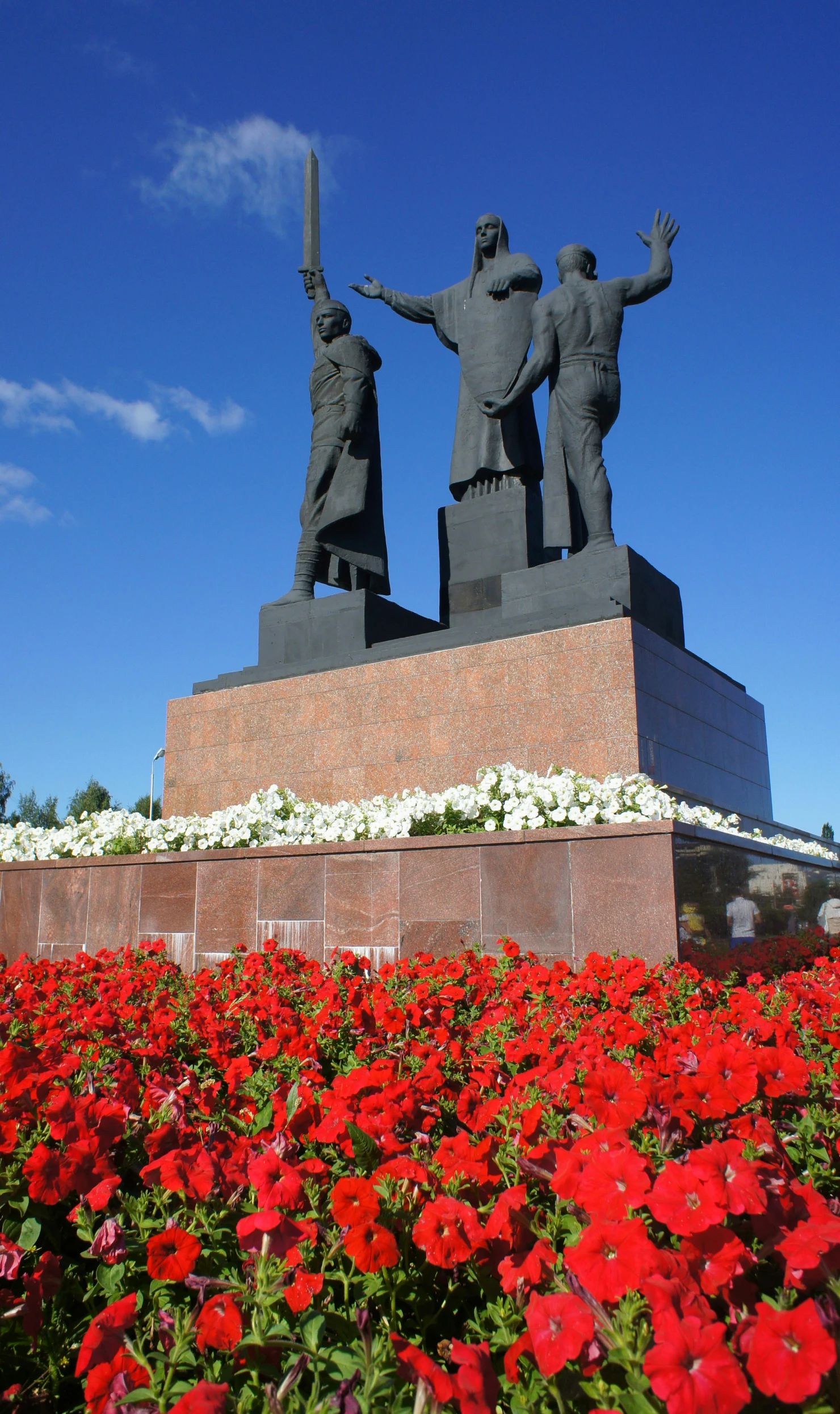 three statues and one of the sculptures in front of a field with red flowers