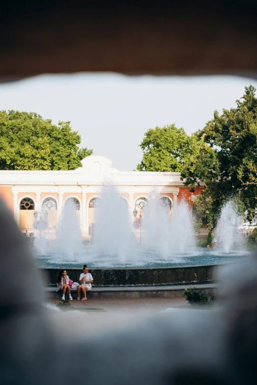 two people sitting on a bench near a fountain