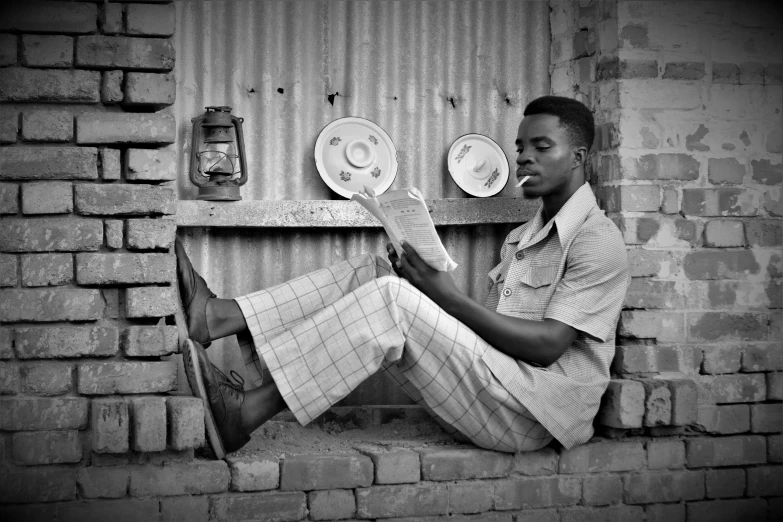 a man sitting on the side of a wall reading a newspaper