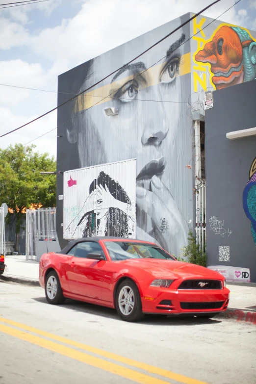 red mustang parked in front of a wall with graffiti