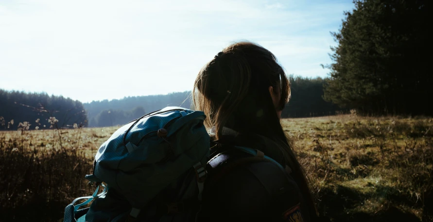 a girl with backpack walking through tall grass