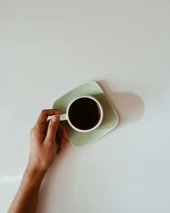 a person holding a cup of coffee on top of a white table