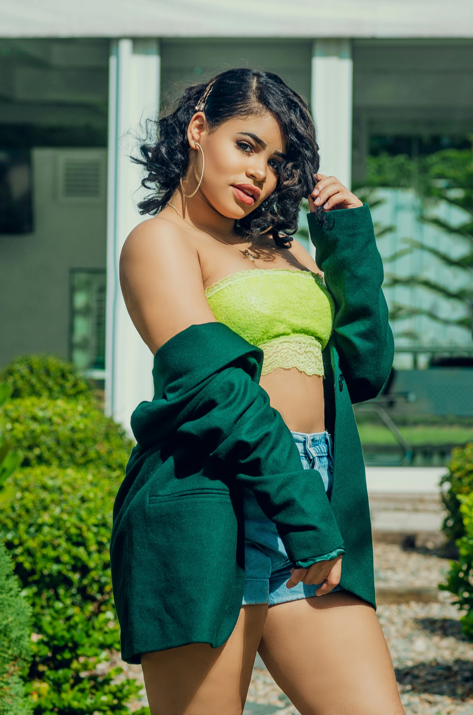 a woman is posing outside in shorts and a green jacket