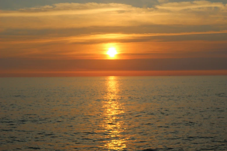 the sun setting over the water off a beach