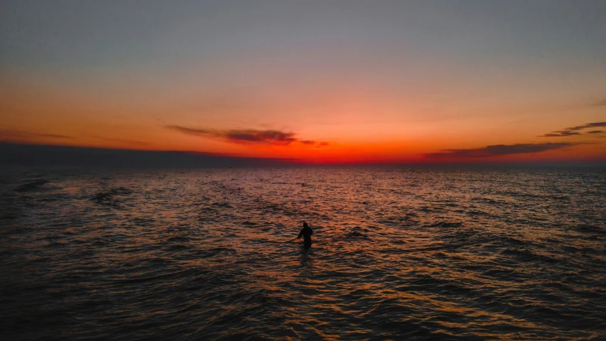 the sun is setting over the ocean with someone standing in the water