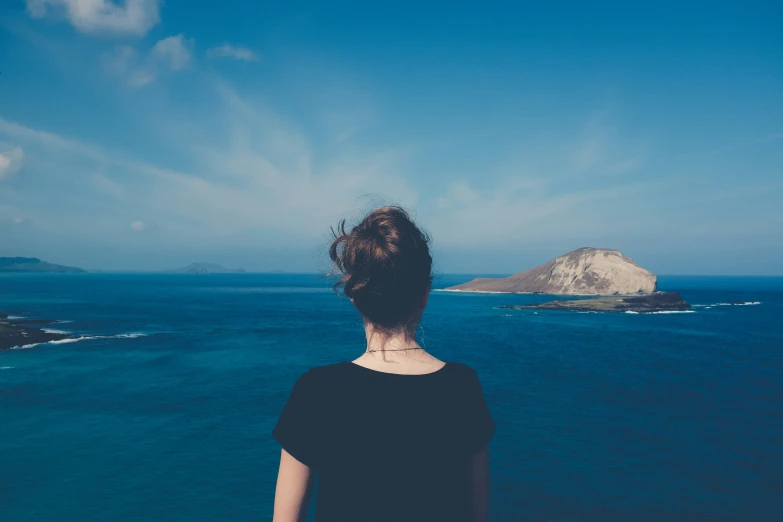 a woman standing at the edge of the ocean staring out at an island