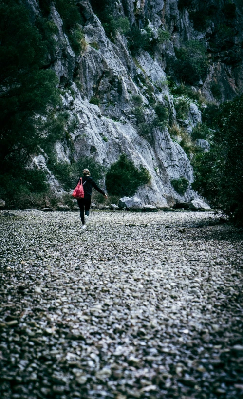 a person walking along a rocky river holding an umbrella