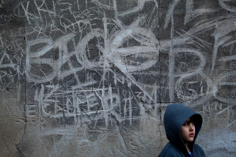 a person in a hooded jacket standing in front of graffiti