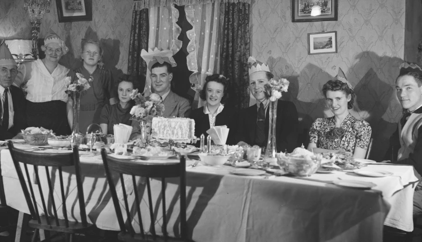 some people sitting around a table with two cakes and glasses on it