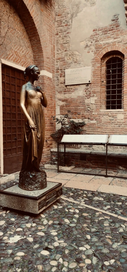 statue of woman near entrance to outdoor building with brick and stone courtyard