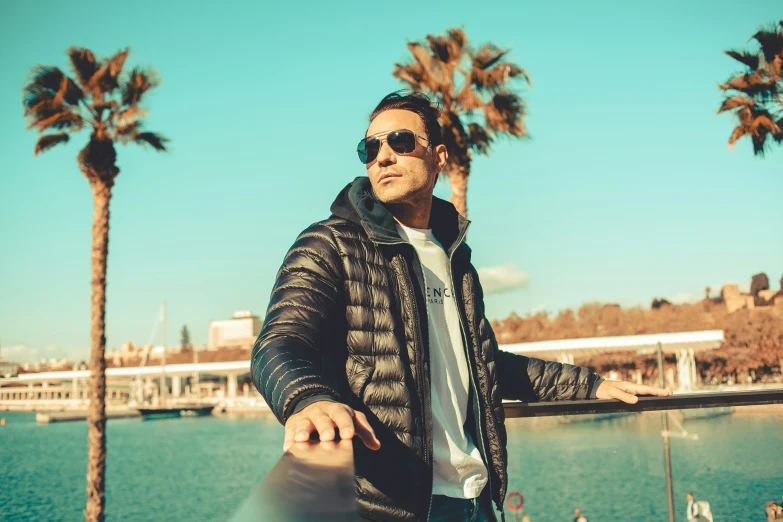 a man wearing sunglasses and a hooded jacket by a lake