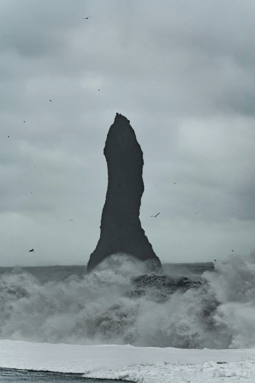 a tall black rock in the ocean on a cloudy day