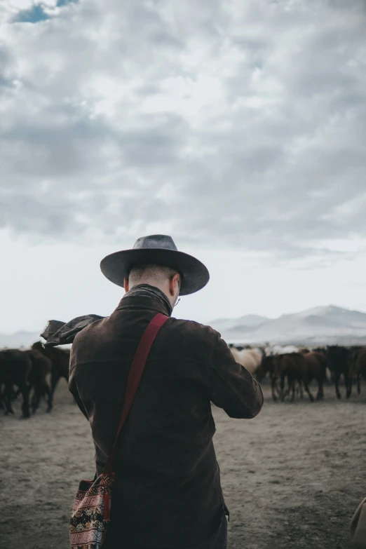 man in hat taking pictures with cows and horses in the background