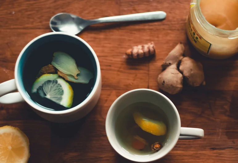 there is an open bottle, tea cup, lemon and ginger with a spoon