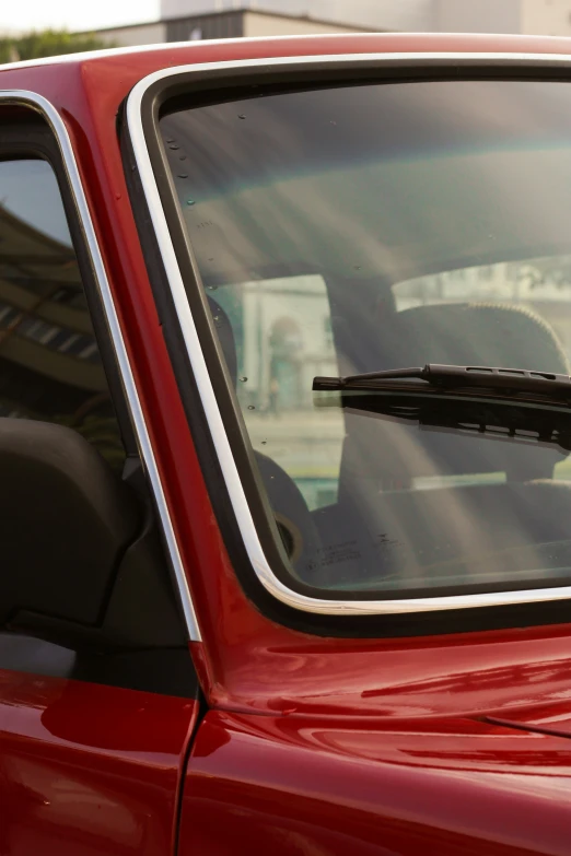 a red car with the sun and buildings in the background