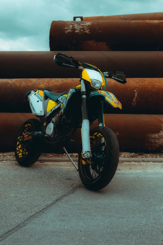 the dirt bike sits parked in front of some big metal pipes