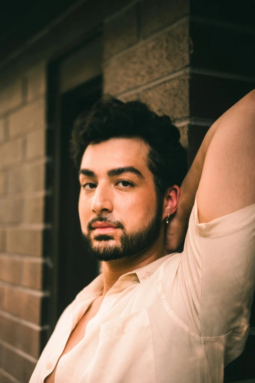 a man in a white shirt stands next to a brick wall