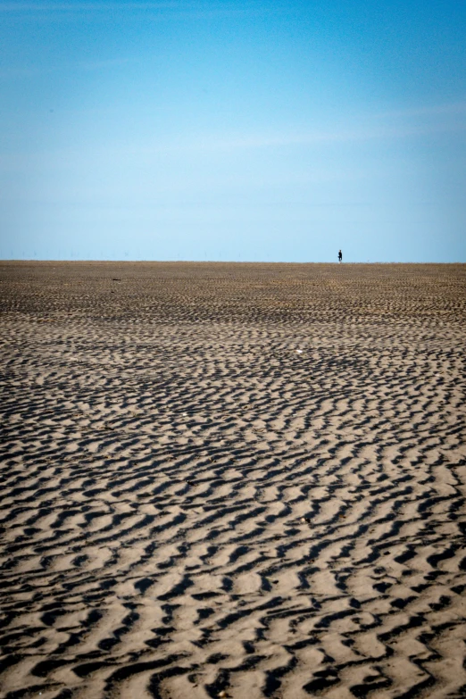 a very large body of sand with a person walking through the distance