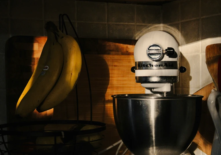 a metal bowl with a mixer and two bananas in a kitchen