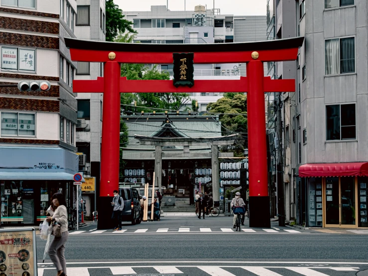 the people walk on the sidewalk by a tall red gate