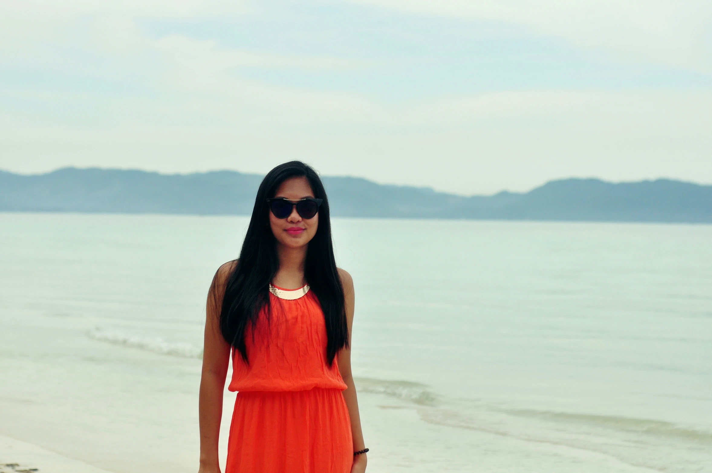 a woman wearing an orange dress is standing near the ocean