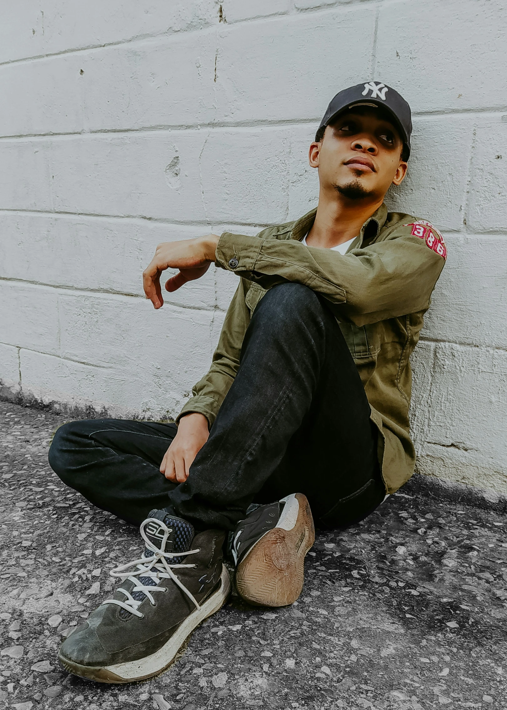 a young man sitting on the ground in front of a white wall