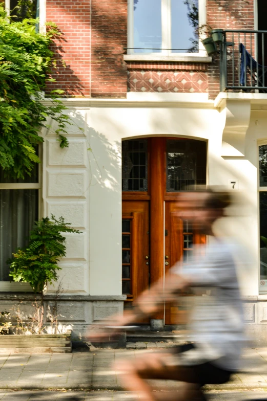 man riding bicycle past a large house in front of it