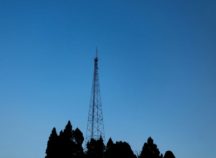 silhouette of radio tower against blue sky with trees