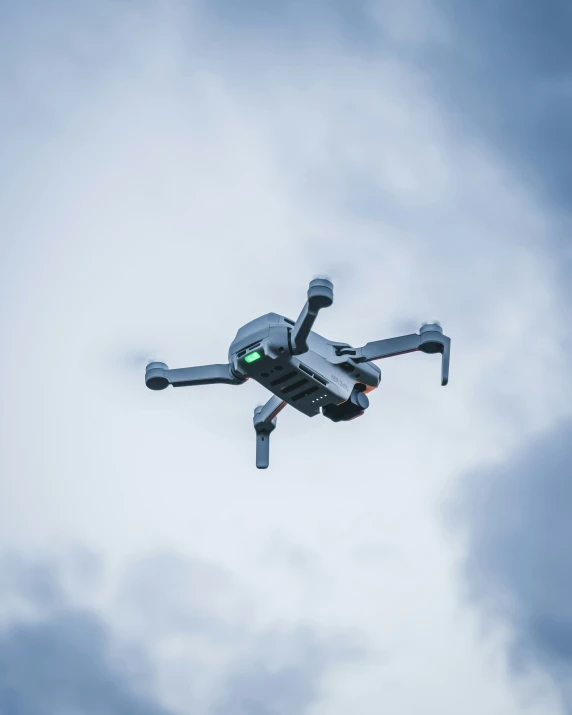 a small gray dji - goggles flying through a cloudy sky