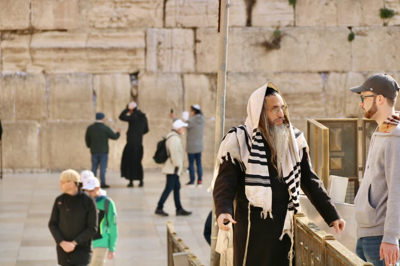 man with long white beard and striped scarf with people walking by on sidewalk