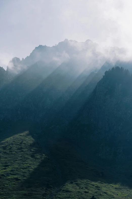 a green field on the side of a mountain under some clouds