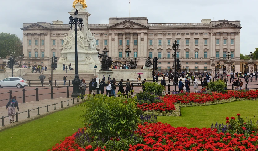 people walking on a path near a building with red flowers in the foreground