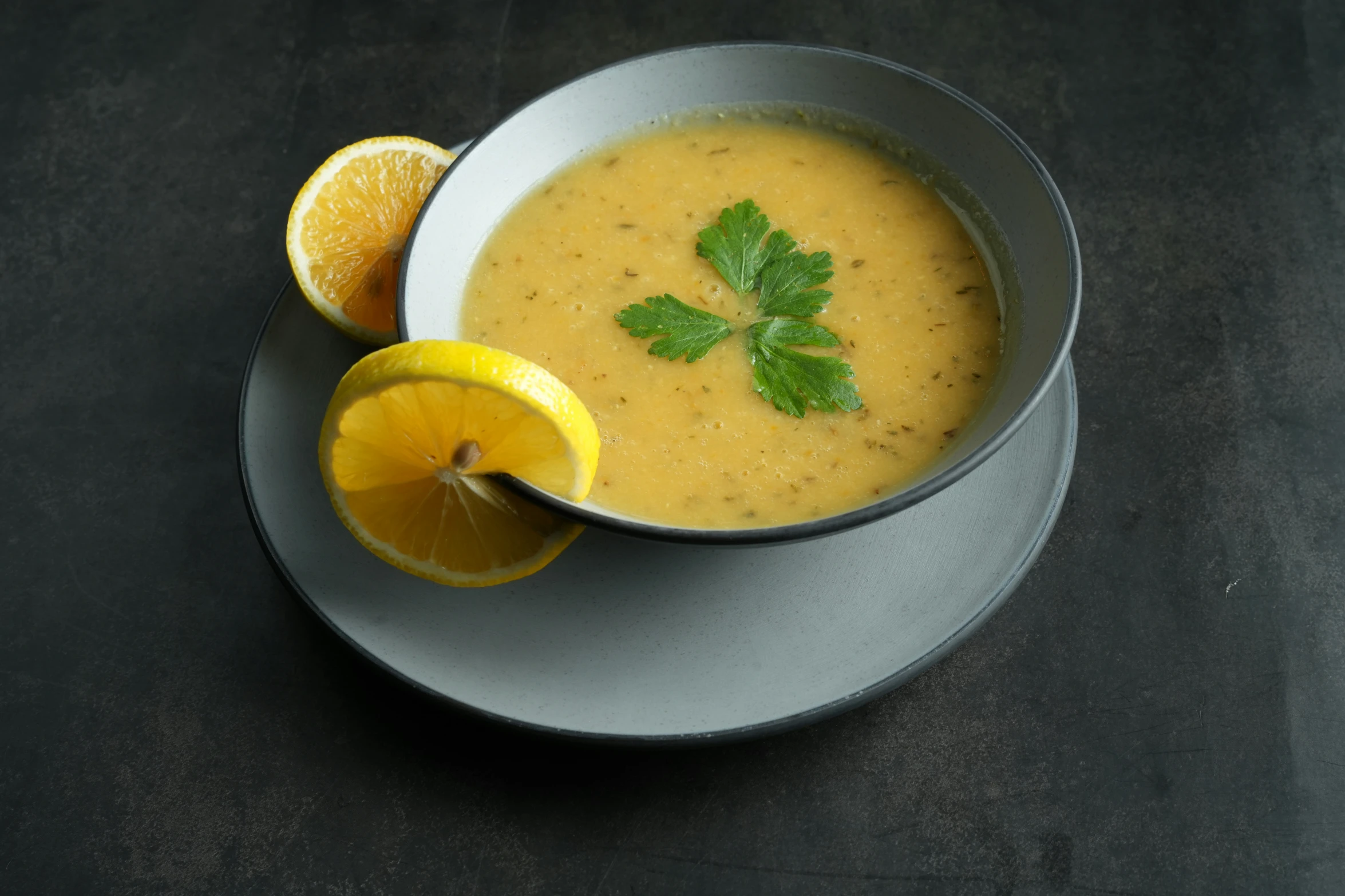 a bowl of soup with sliced lemon and green leaves