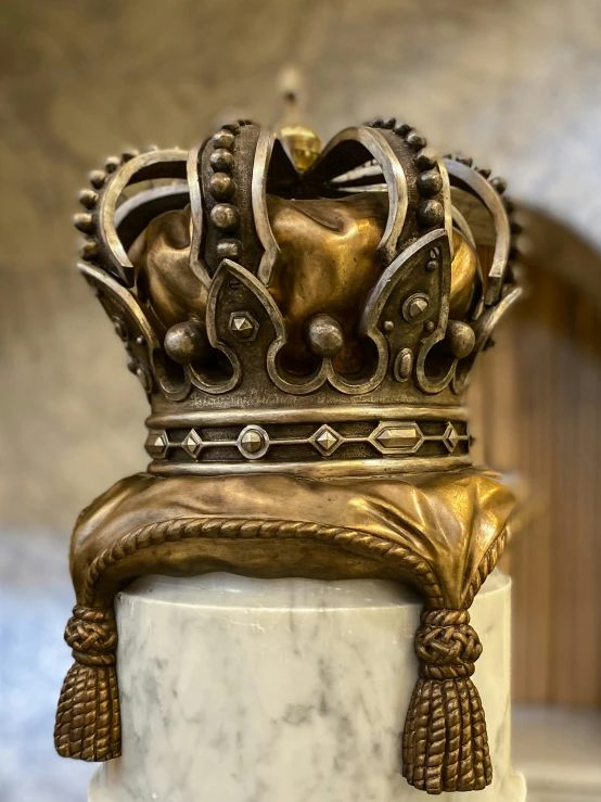 a gilded gold crown is on top of a white pillar