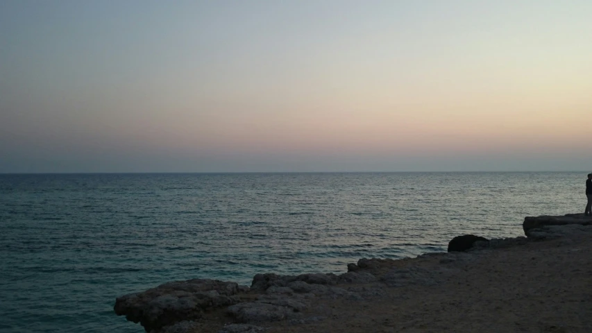 the water has a blueish sky and two benches next to it