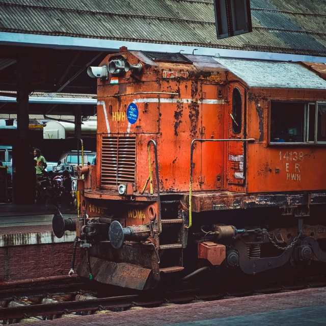 an old rusty red train parked on tracks in front of an abandoned building