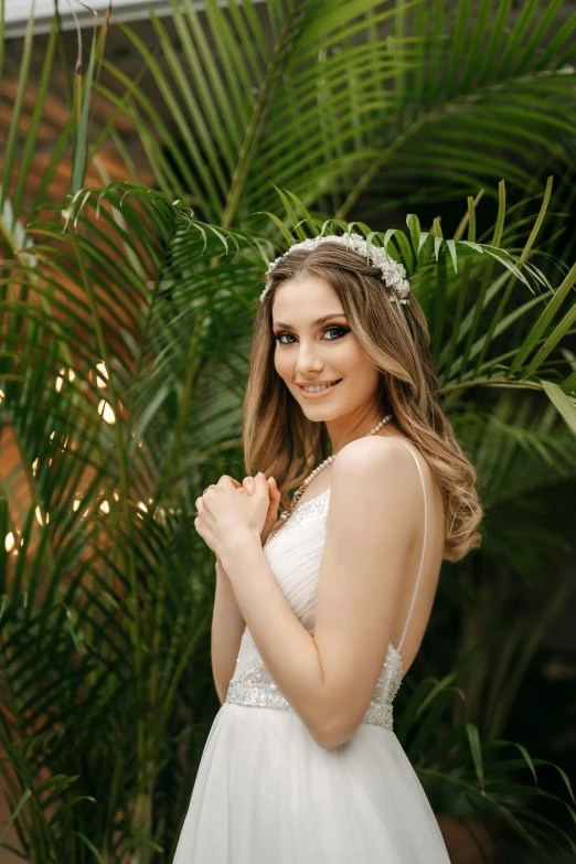 a woman wearing a wedding dress poses in front of a plant