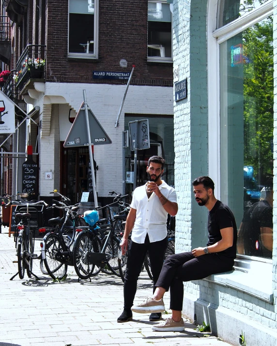 two men sit on a wall outside of store windows