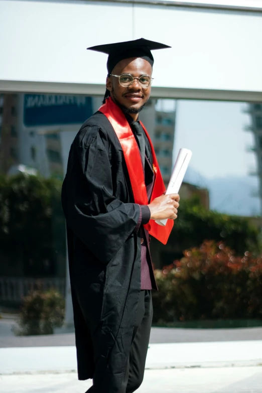 a man dressed up in a graduation gown with a red sash and graduate cap